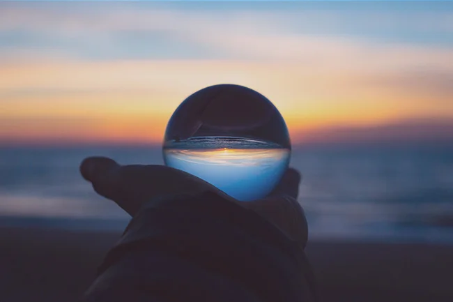A person holding a crystal ball in their hand. The image symbolizes the concept of using Neville Goddard's “I remember when” technique to create your desired future.