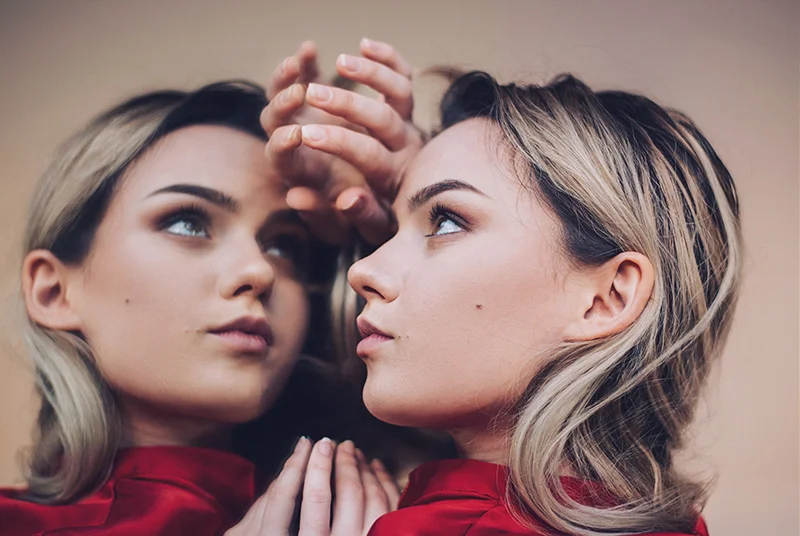 A woman in a redd dress is looking into a large mirror. This image shows how the mirror manifestation method can help you manifest your desires.